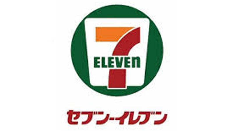 白地に緑の円形の枠、その中にオレンジと赤の配色で描かれた数字の「7」と、中央を横切る「ELEVEN」の文字。下部には赤いカタカナで「セブン-イレブン」と表記された公式ブランドロゴ。