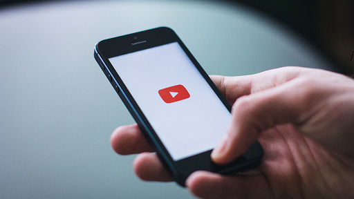 スマートフォンの画面にYouTubeの赤い再生ロゴが表示されている様子。片手で端末を保持しており、動画配信サービスの利用やモバイル視聴のスタイルを具体的に示しています。